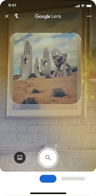 En un teléfono, se abre la app de Google Lens. Una notificación indica que la usuaria puede presionar el botón del obturador para buscar una imagen de esculturas de manos de piedra grandes en un desierto.